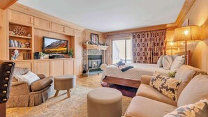 A cozy room with a fireplace, a television, a sofa, and a bed. - Cozy Studio with Fireplace, King Bed, A/C (Ellicottville)
