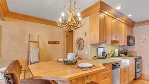 A kitchen with wooden cabinets, a central island, a chandelier, and a microwave. - Cozy Studio with Fireplace, King Bed, A/C (Ellicottville)