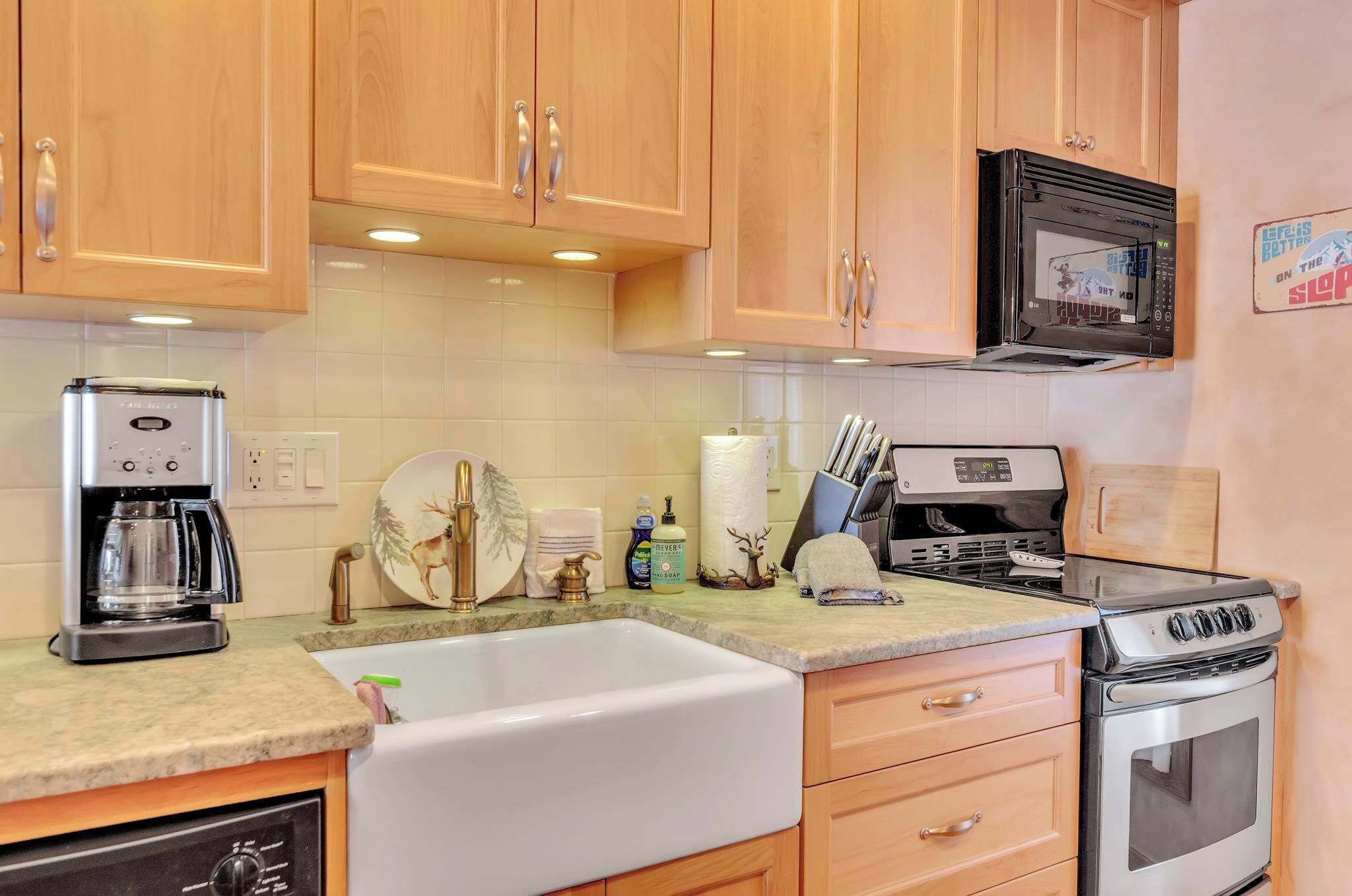 A kitchen with wooden cabinets, a microwave, a coffee maker, a sink, and a stove.