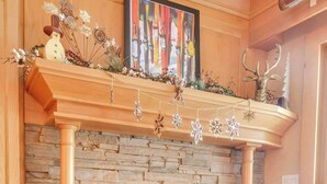 A fireplace with a stone surround, a mantel with a framed artwork, and a decorative snowflake hanging above. - Cozy Studio with Fireplace, King Bed, A/C (Ellicottville)