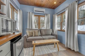 A cozy room with a sofa, a wooden table, and a kitchen area with a refrigerator.