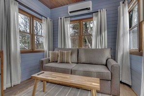 Una habitación con un sofá, una mesa de centro de madera y una ventana con cortinas.