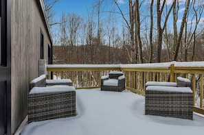 A covered outdoor deck with wicker furniture and snow on the ground.
