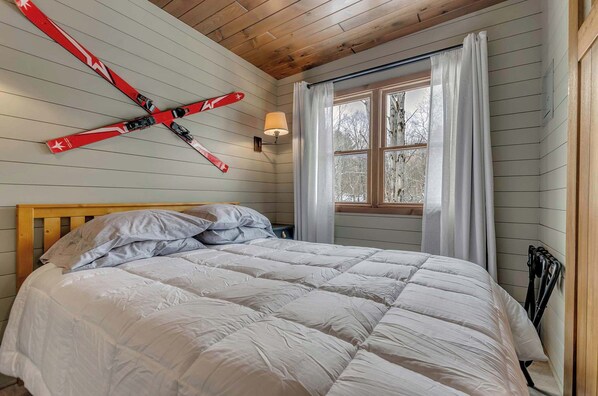 A bedroom with a bed, wooden headboard, a window with curtains, and a ski-themed wall decoration.