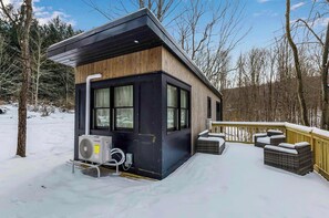 Eine moderne Holzhütte mit Terrasse, Sitzgelegenheit im Freien und einer Klimaanlage.