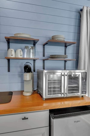 A kitchen with a built-in toaster oven, a coffee maker, and shelves with dishes and glasses.
