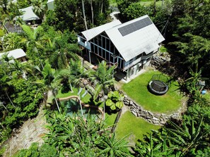 Vista aérea de una casa moderna rodeada de exuberante vegetación, con piscina y trampolín.