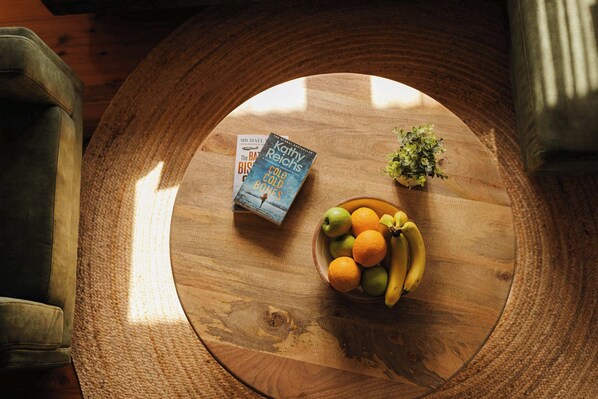 A round wooden table with a bowl of fruit and a book.