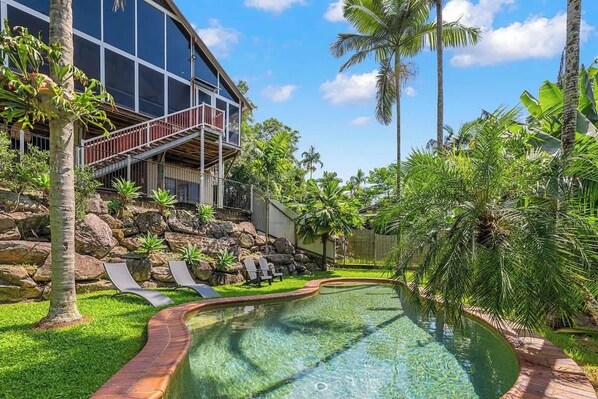 Una casa moderna con piscina, rodeada de abundante vegetación y palmeras.