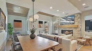 A spacious living area with a wooden dining table, comfortable seating, a stone fireplace, and a large window offering a view of the outdoors. - Old Town Alpine Vista: Near Park City Ski Resort (Park City)