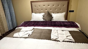 A neatly made bed with a tufted headboard, white and brown bedding, a purple throw blanket, and folded towels on the bed. - Oasis Retreat Cottages Pangong (Leh)