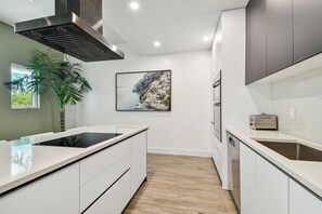 A modern kitchen with white cabinetry, a stainless steel range hood, and a large window.