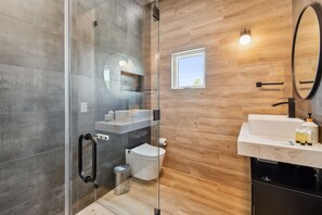 A modern bathroom with a glass shower enclosure, a toilet, a sink with toiletries, and a mirror.