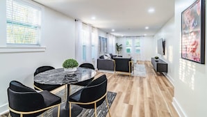Ein modernes Wohnzimmer mit Essbereich, mit einem Marmortisch, schwarzen Stühlen, einer Couch und einem Fernseher.