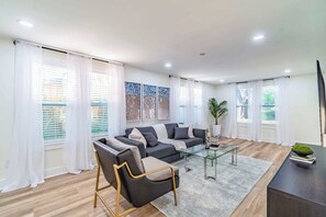 Ein modernes Wohnzimmer mit Sofa, Sessel, Glastisch und einem TV-Schrank.