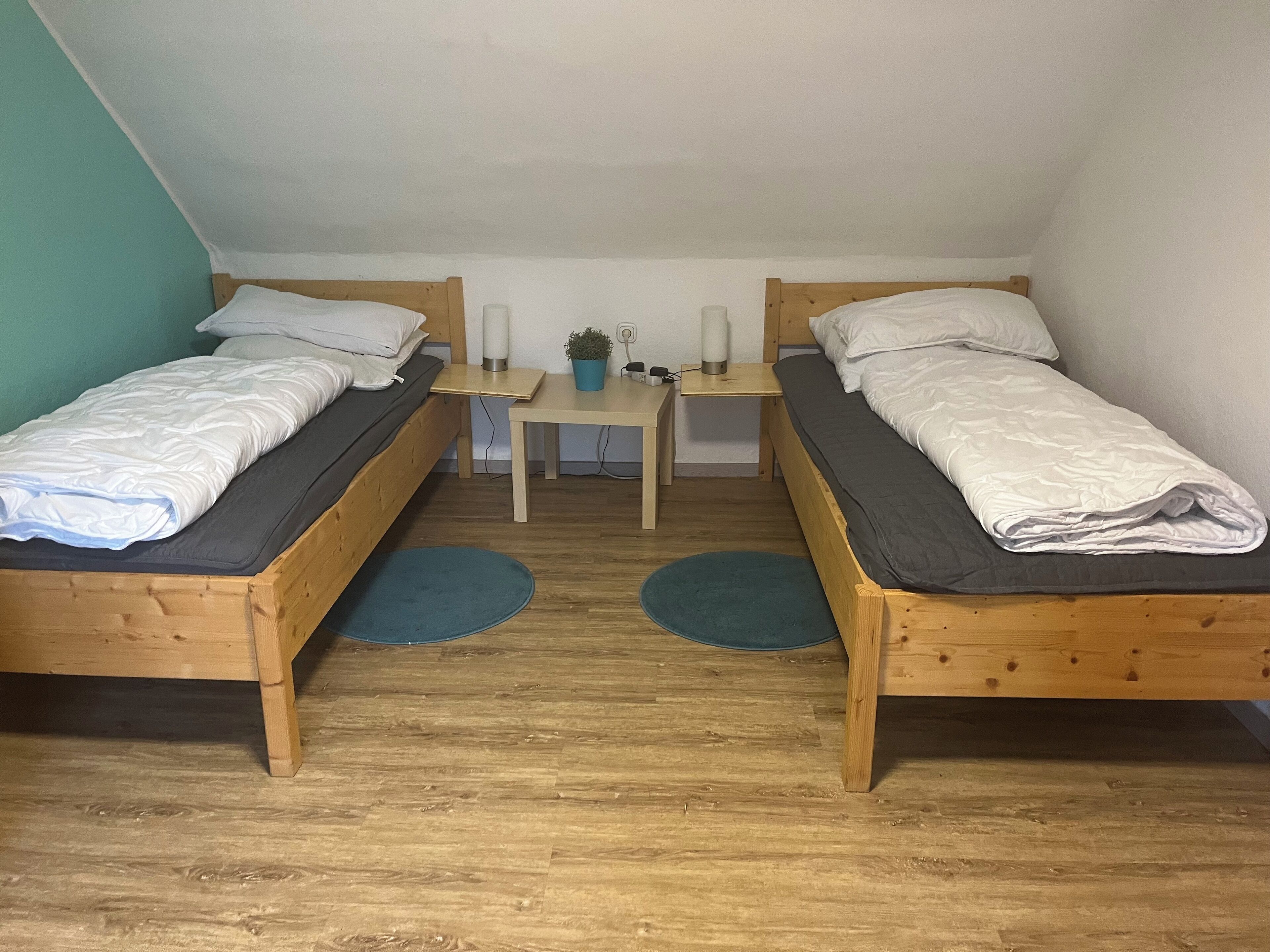 A small, cozy room with two wooden beds, a small table, and a potted plant.