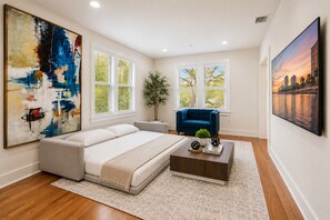 A modern bedroom with a bed, a blue armchair, a coffee table, and a large abstract painting.