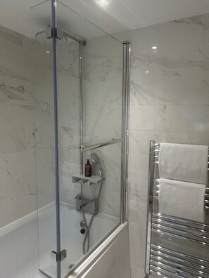 Un baño moderno con ducha acristalada, toallero integrado y pared revestida de mármol.