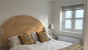 Une chambre à coucher avec un grand lit, deux oreillers, une lampe de chevet, une fenêtre avec des stores et un radiateur.
