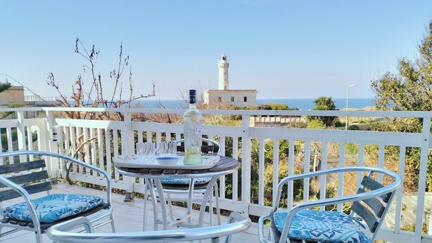 A terrace with metal chairs and a table, overlooking a coastal area with a lighthouse in the background. - Villa historic center sea view (Anzio)