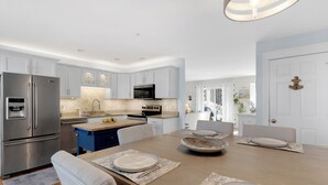 Una cocina moderna con armarios blancos, electrodomésticos de acero inoxidable y una mesa de madera dispuesta para cuatro personas.