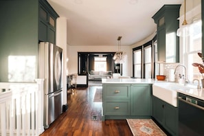 Une cuisine moderne avec des meubles de couleur vert foncé, des appareils en acier inoxydable et un grand îlot central.
