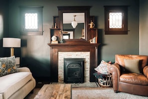 Un salon avec une cheminée, un canapé, un fauteuil en cuir et une lampe.