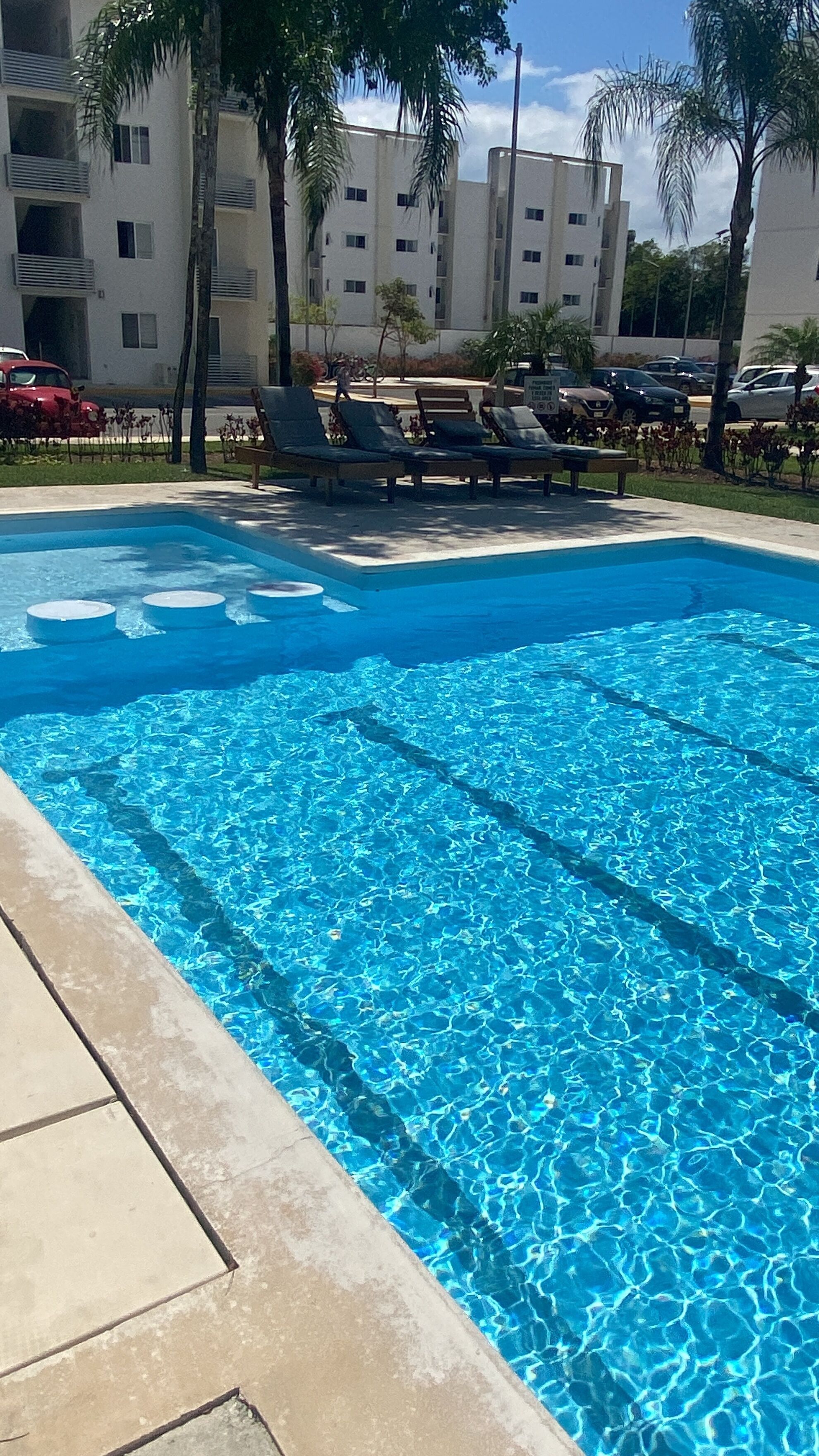 A clear blue pool with lounge chairs and palm trees. - Beach, your apartment near the sea and the Mayan Train (Playa del Carmen)