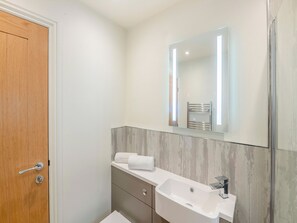 A modern bathroom with a wooden door, a white sink, a mirror, and a towel rack.