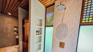 A modern bathroom with a shower, a wooden shelf with toiletries, and a geometric patterned wall. - Serenity Wave Bungalow (Cahuita)