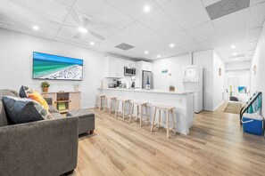 A modern kitchen with a large island, bar stools, and a flat-screen TV displaying a beach scene.
