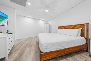 Ein Schlafzimmer mit einem Holzbett, weißen Wänden und einem Deckenventilator.