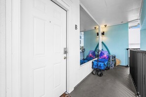 A hallway with a white door, a blue wall, and a security camera. There are blue luggage carts with a surfboard and a beach-themed chair. - Perfect Cozy Island Get-Away on Siesta Key! (Siesta Key)