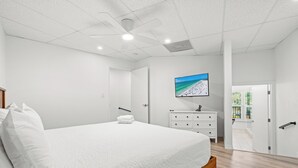 A modern bedroom with a large bed, a white dresser, a flat-screen TV, and a door leading to a balcony. - Perfect Cozy Island Get-Away on Siesta Key! (Siesta Key)