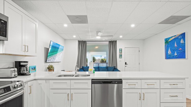 A modern kitchen with white cabinetry, a stainless steel dishwasher, and a flat-screen TV. - Perfect Cozy Island Get-Away on Siesta Key! (Siesta Key)
