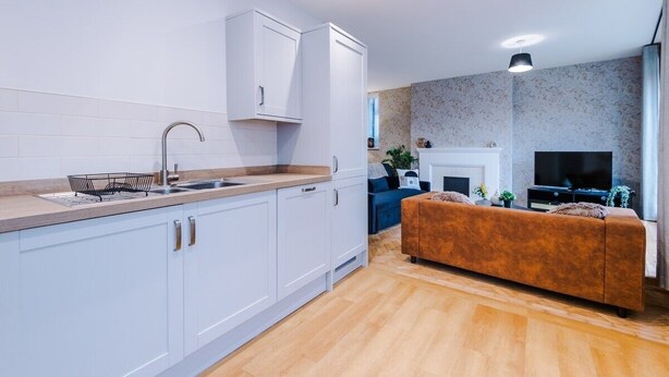 A modern kitchen with white cabinets, a sink, and a countertop. There is a living area with a sofa and a TV. - Central York Penthouse With Private Roof Terrace (York)