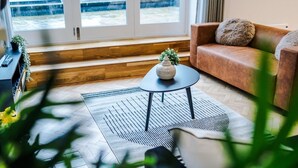 A modern living room with a sofa, a small round table with a plant, and a view through large windows. - Central York Penthouse With Private Roof Terrace (York)