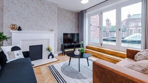 A modern living room with a fireplace, a television, and a large window with a city view. - Central York Penthouse With Private Roof Terrace (York)