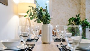 A dining table set with white plates, silverware, and clear wine glasses, centered with a white vase containing green foliage. - Central York Penthouse With Private Roof Terrace (York)