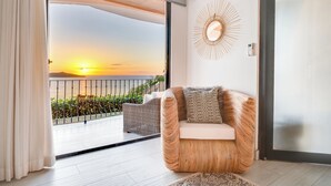 A modern living room with a view of the sunset, a wicker chair, and a decorative wall piece. - Romantic Getaway with Stunning Panoramic Ocean Views, Amazing Sunsets (Playa Flamingo)