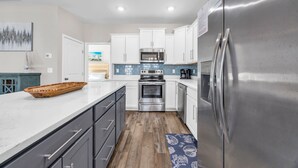 A modern kitchen with white cabinets, stainless steel appliances, and a wooden floor. - Spacious 5-bedroom house with a quick walk or golf cart ride to the beach (Myrtle Beach)