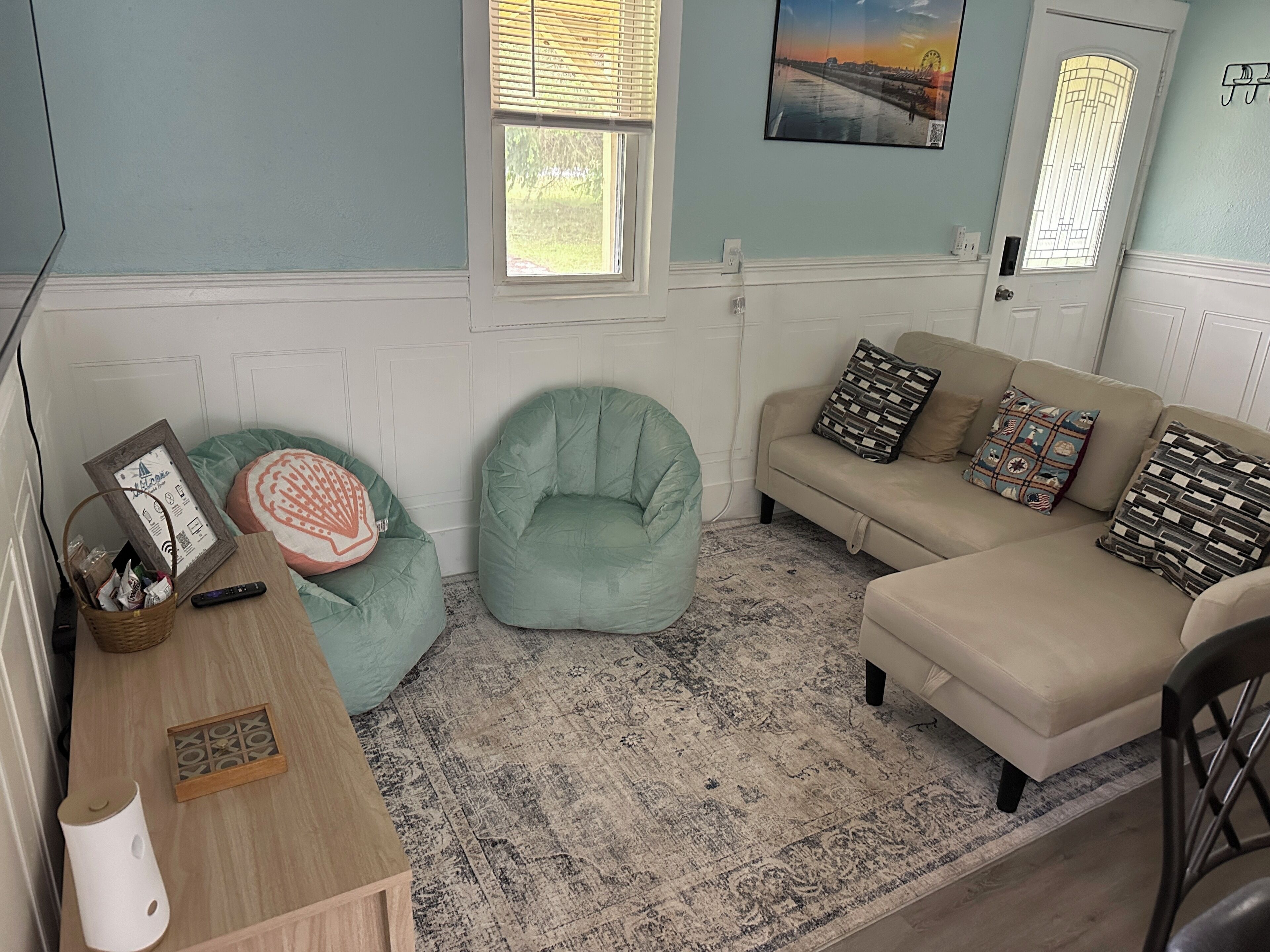 A living room with a light blue wall, a beige sofa, a green bean bag chair, and a patterned rug.