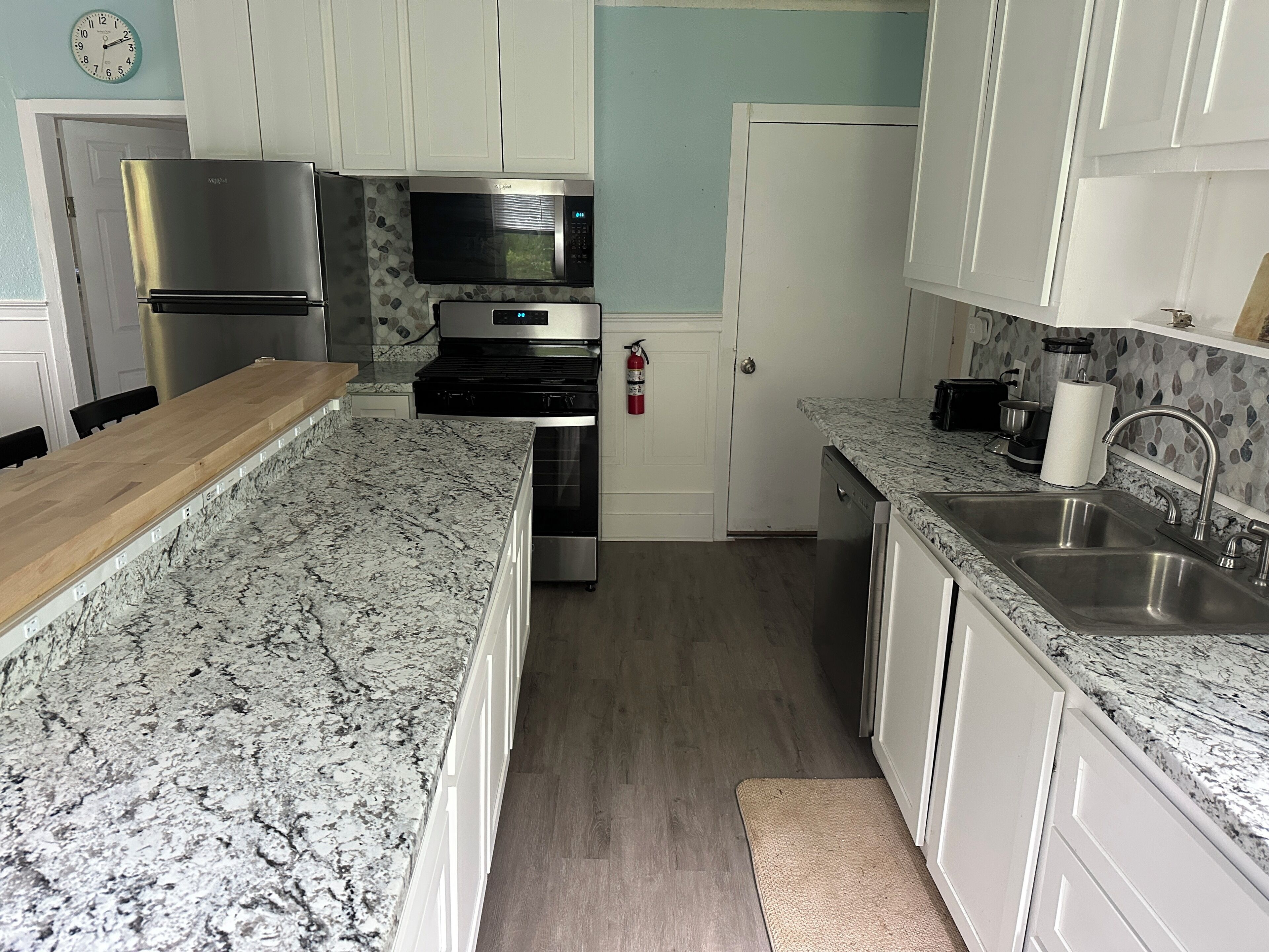 Une cuisine avec des meubles blancs, des plans de travail en granit, des appareils électroménagers en acier inoxydable et une table à manger en bois.