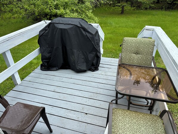 A wooden deck with a covered grill, two chairs, and a table.