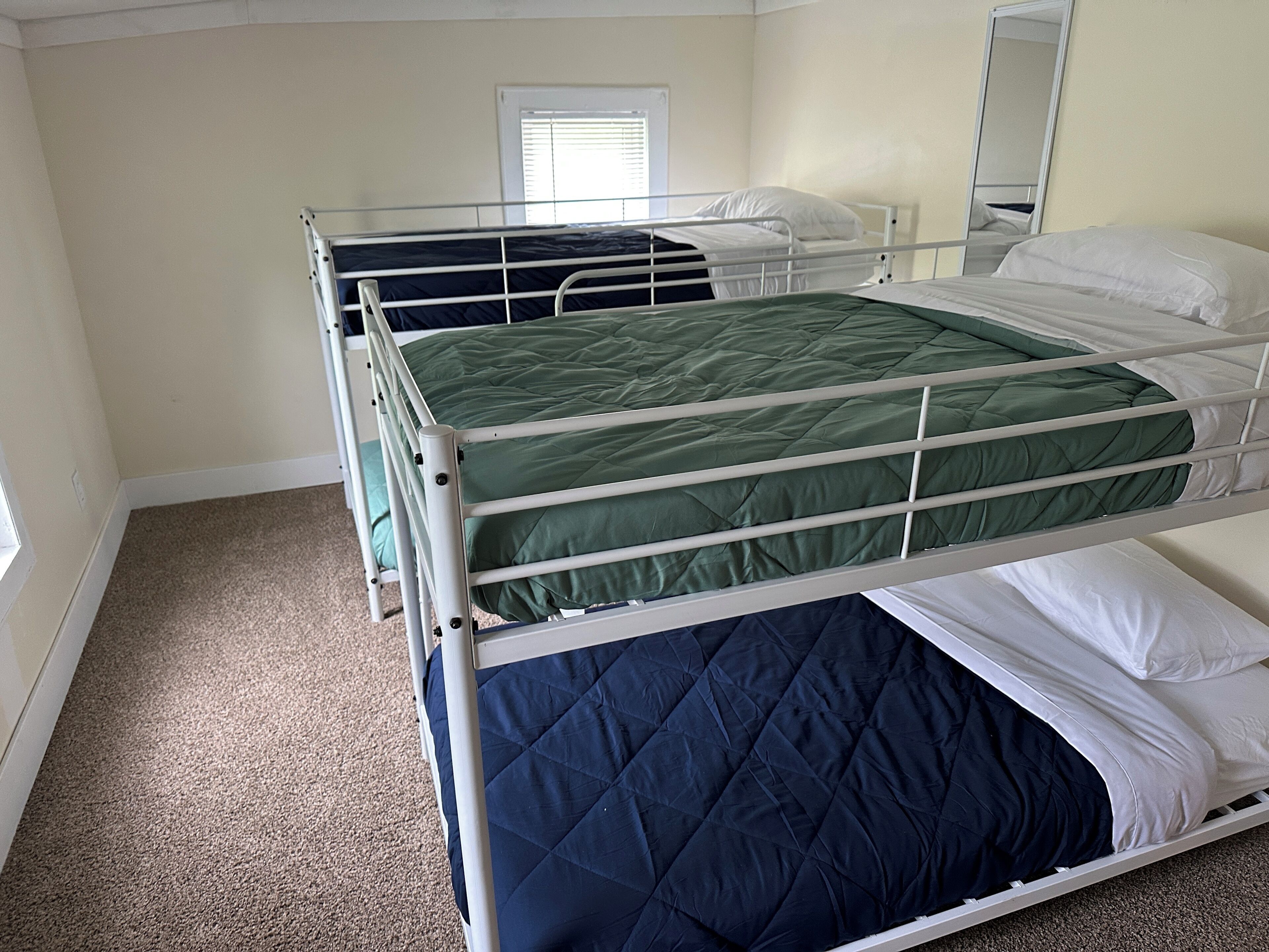 A room with bunk beds, a window with blinds, and a mirror on the wall.