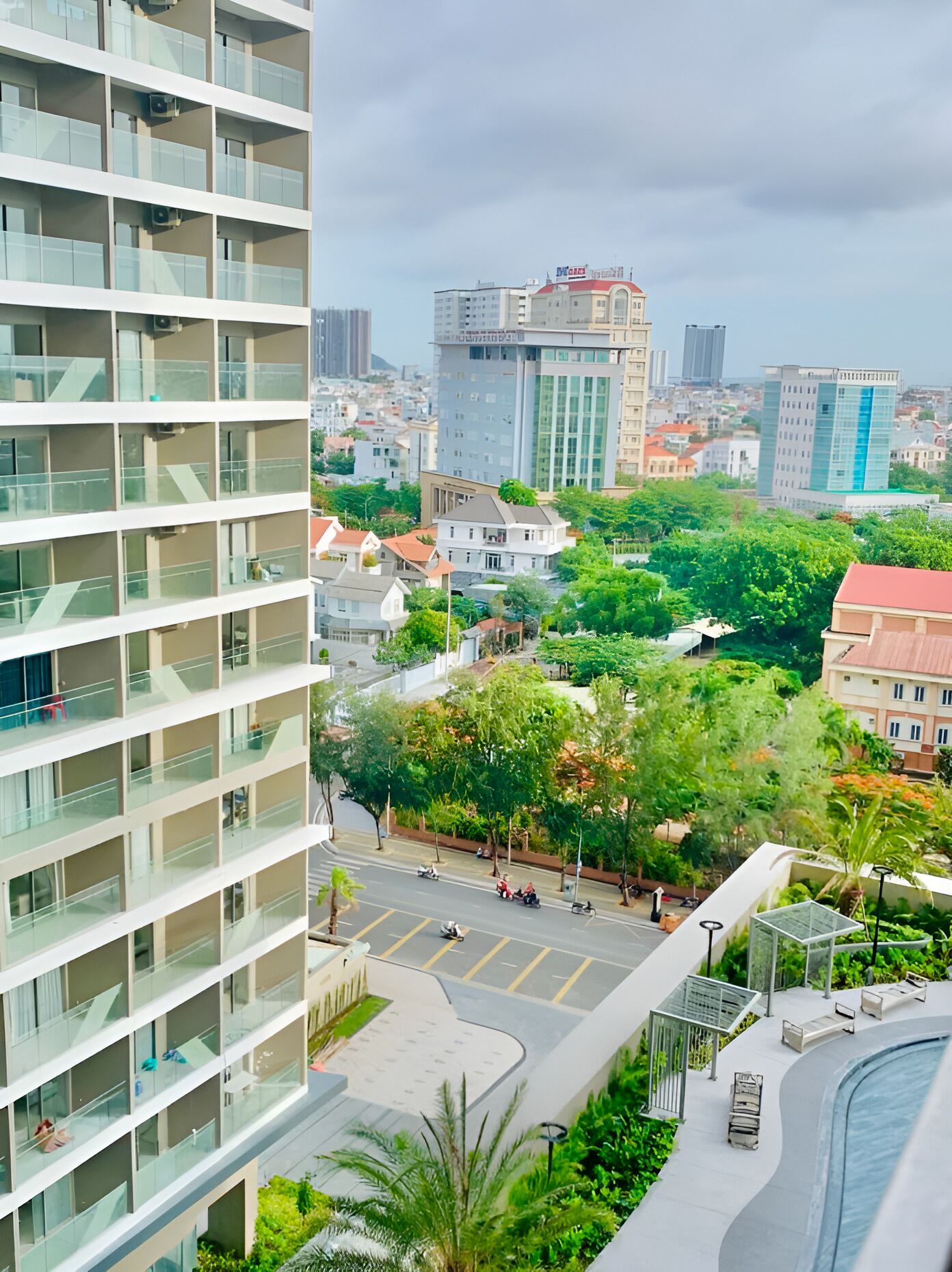 A high-rise building with multiple balconies, a central courtyard with trees, and a view of surrounding urban buildings.