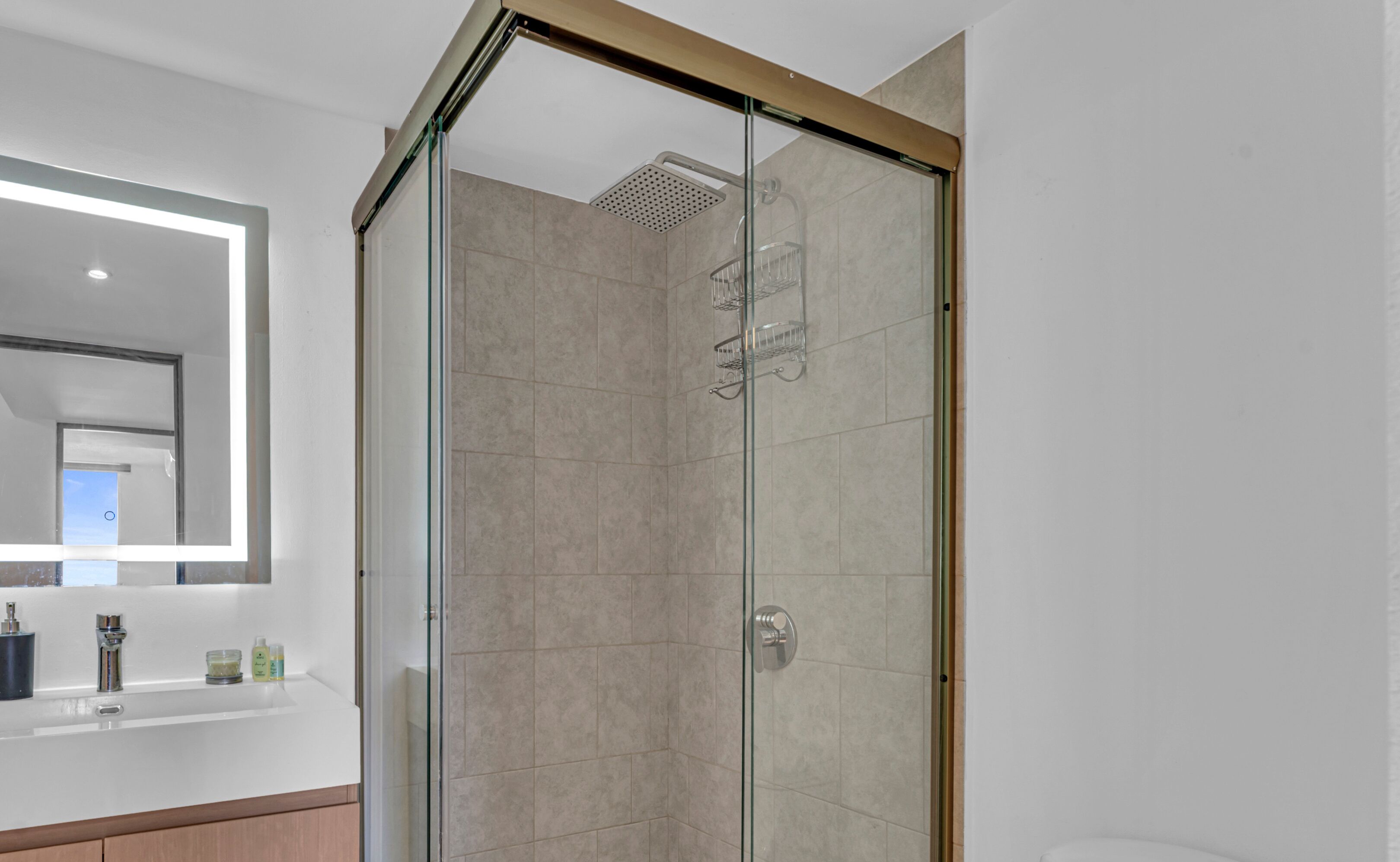Un baño moderno con cabina de ducha de vidrio, un espejo grande y encimera blanca con artículos de aseo.