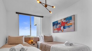 A modern hotel room with two beds, a large window, a ceiling light fixture, and a colorful abstract painting on the wall. - Cozy, Modern, Upscale APT W/Views, Pool, Gym, A/C (San Salvador)