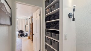 A hallway with a white door, a wall-mounted light fixture, and shelves with gray storage bins. - Woodsy, Quiet Neighborhood, 2 bedroom (Grants Pass)