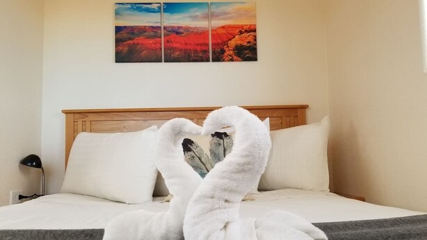 A bed with white pillows and a blanket, a wall-mounted painting, and a lamp on a bedside table. - Affordable Getaway near Grand Canyon Sleeps 4 (Williams AZ 86046)